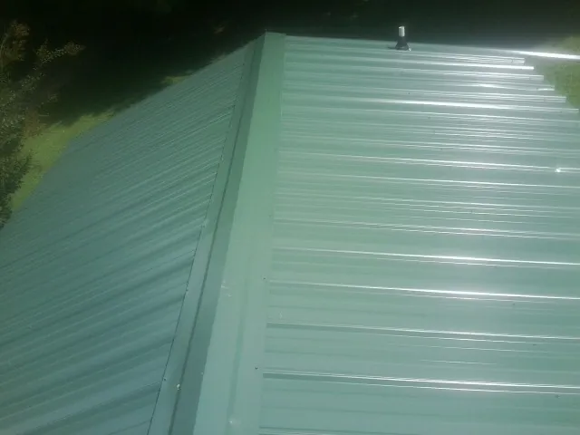 New green metal panels meeting at the ridge of a roof — Flat Roof Repair work by our crew in Newbury
