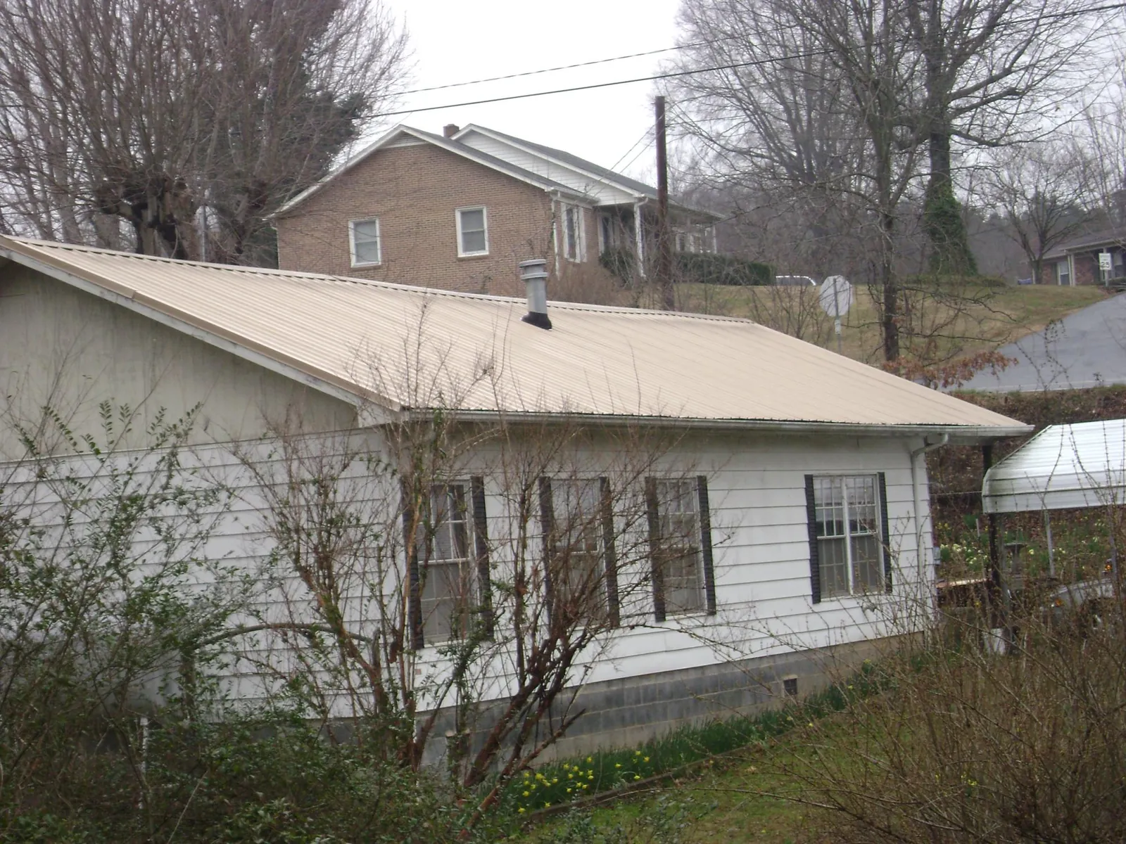 Tan metal roof on a white sided house set into a hillside — Commercial Roofing by Roofing Brothers in Newbury